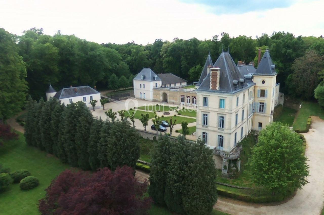 Vue aérienne d'un château entouré de jardins, d'arbres et d'une cour centrale avec une voiture stationnée.