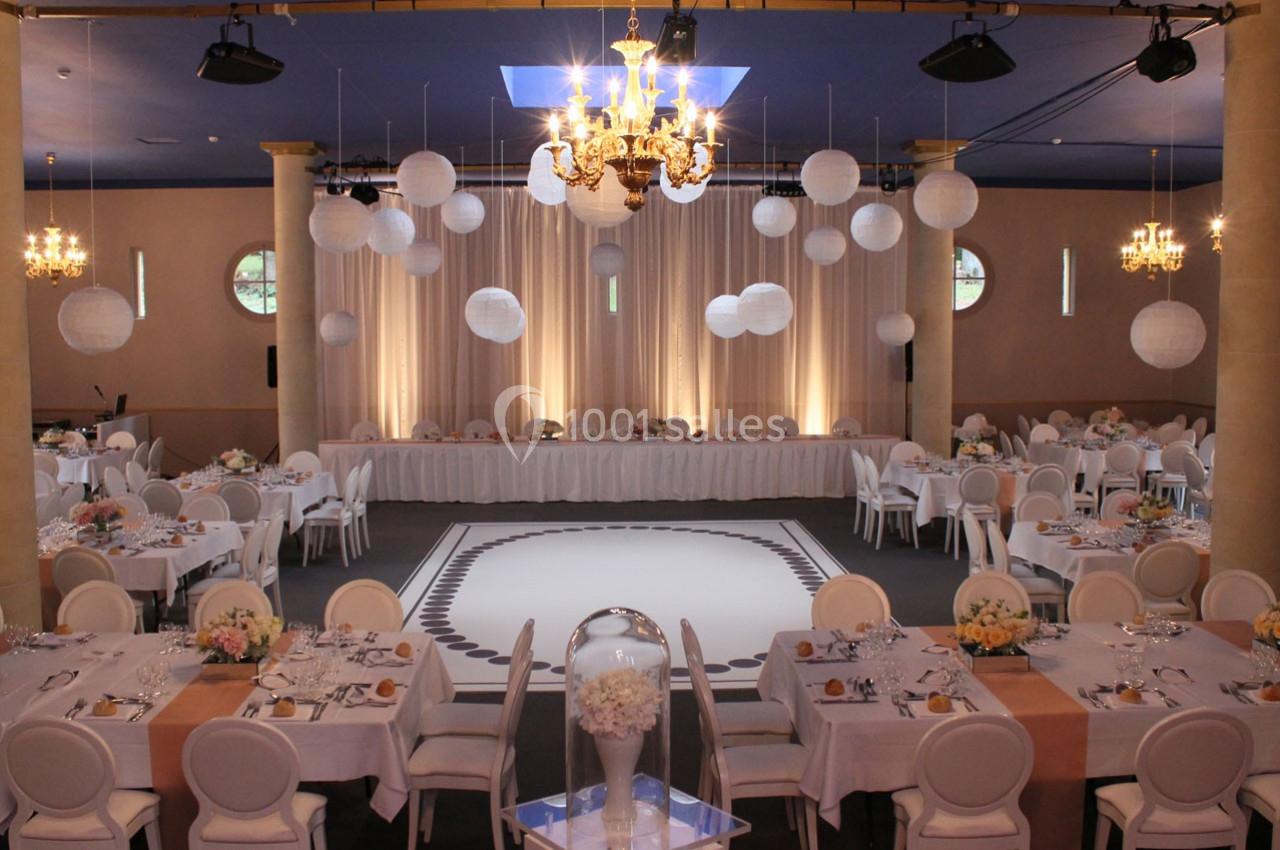 Salle de réception élégante décorée de lanternes blanches suspendues, tables dressées et éclairage chaleureux.