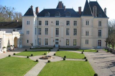 Façade d'un château entouré de jardins bien entretenus, avec un ciel nuageux en arrière-plan.
