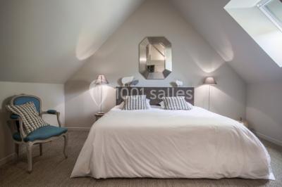 Dortoir lumineux avec plusieurs lits simples alignés, draps blancs et cartes géographiques accrochées aux murs.