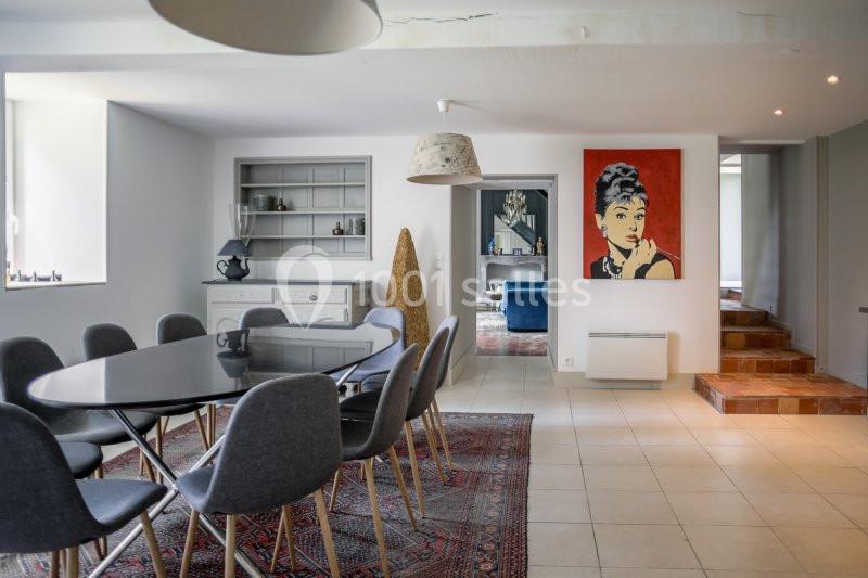 Salle à manger moderne avec table noire, chaises grises, tapis coloré et tableau mural représentant une femme.
