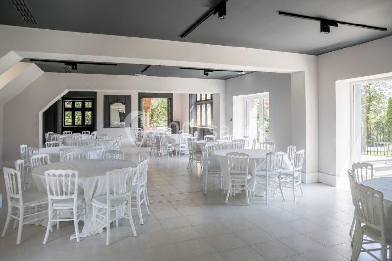 Salle lumineuse avec tables rondes recouvertes de nappes blanches et chaises assorties, grandes fenêtres donnant sur l…