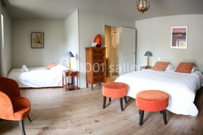 Dortoir lumineux avec plusieurs lits simples alignés, draps blancs et cartes géographiques accrochées aux murs.