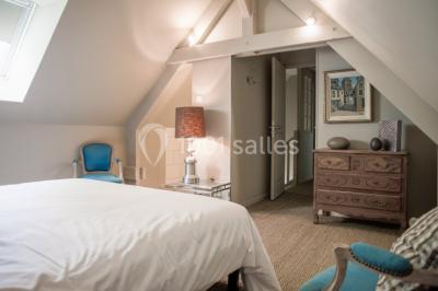 Dortoir lumineux avec plusieurs lits simples alignés, draps blancs et cartes géographiques accrochées aux murs.