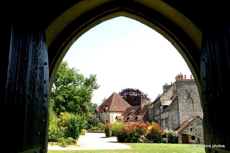 Vue d'un village avec des bâtiments en pierre et des toits en tuiles, encadrée par une arche en bois sombre.