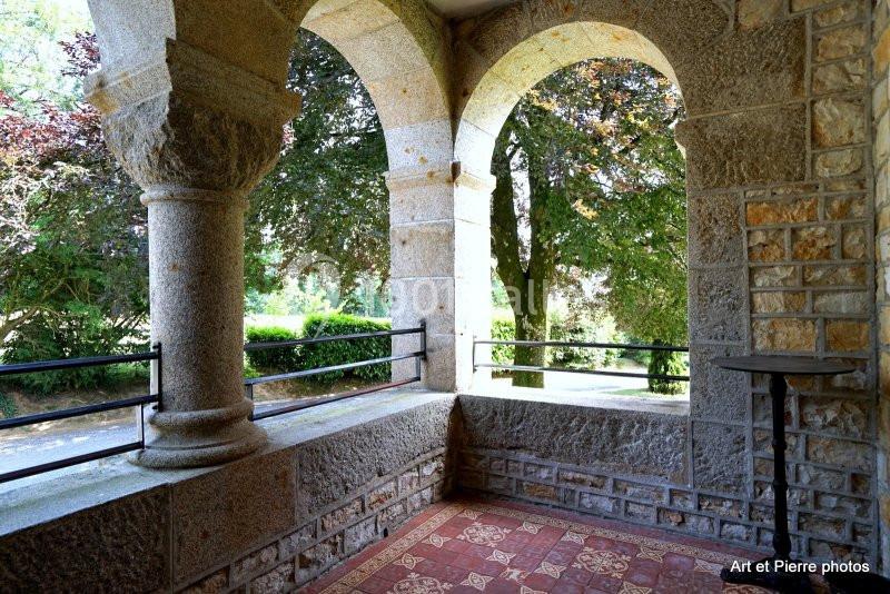Terrasse en pierre avec arches ouvertes, carrelage ancien et vue sur un jardin arboré.