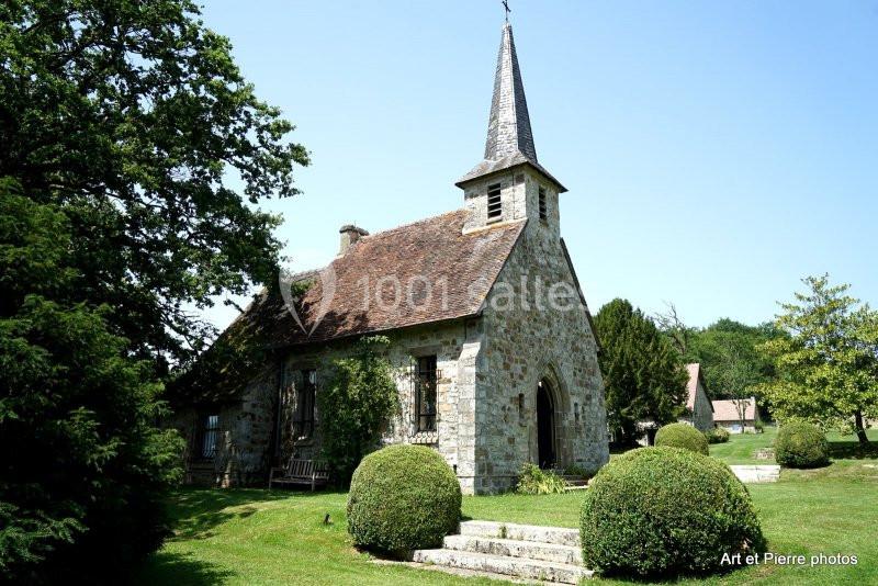 Petite église en pierre entourée de verdure, avec un clocher pointu et un jardin arboré.