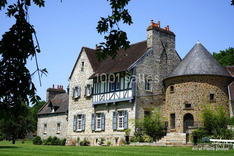 Maison en pierre avec colombages et tour ronde, entourée de verdure sous un ciel dégagé.