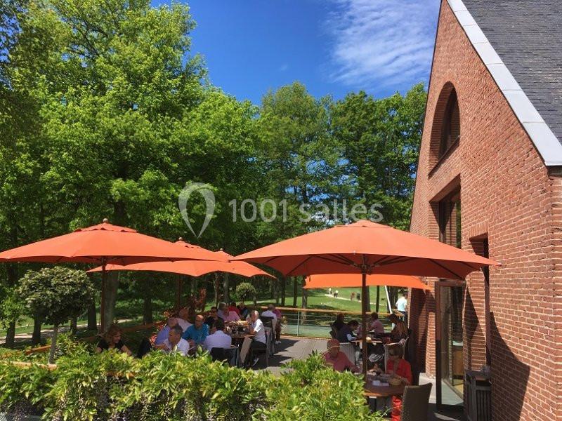 Terrasse d'un restaurant avec des parasols orange, entourée de verdure et baignée de soleil.