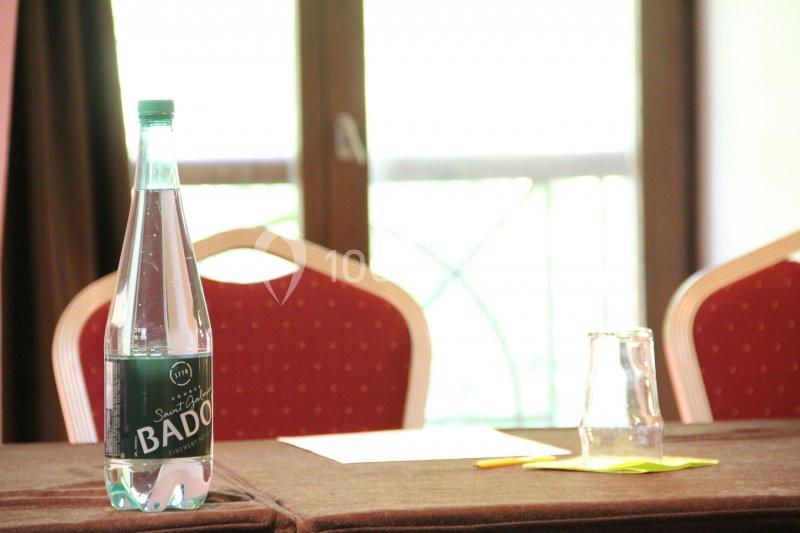 Bouteille d'eau minérale posée sur une table avec un verre, un stylo et des documents, devant une fenêtre.