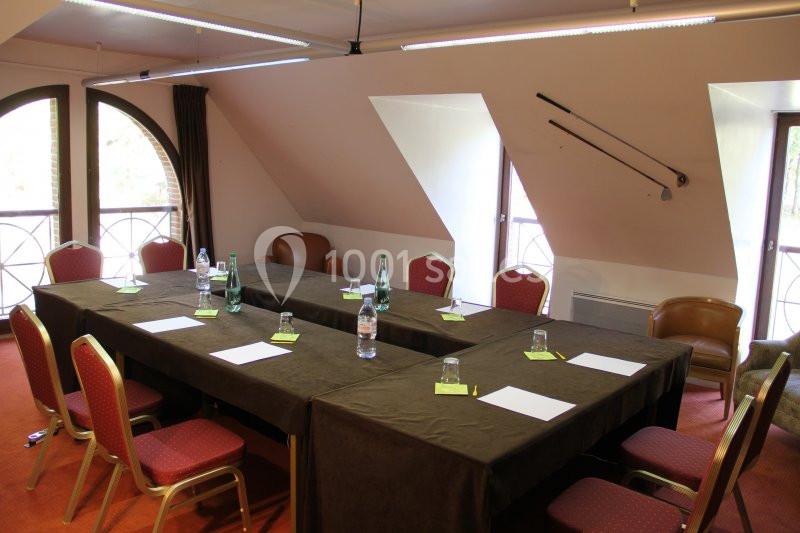Salle de réunion lumineuse avec table en U, chaises rouges, bouteilles d'eau et documents sur une nappe sombre.