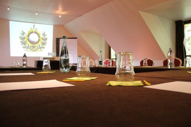 Salle de réunion avec tables couvertes de nappes sombres, verres, bouteilles d'eau et écran de projection allumé.