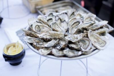 Vue nocturne d'une maison en bois éclairée, entourée d'arbres illuminés, sous un ciel nuageux avec la lune visible.