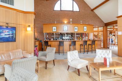 Vue nocturne d'une maison en bois éclairée, entourée d'arbres illuminés, sous un ciel nuageux avec la lune visible.