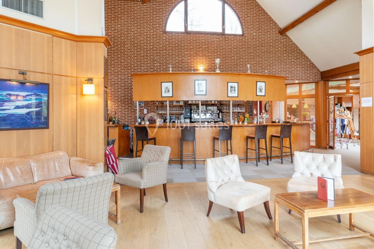 Intérieur d'un salon avec des fauteuils, un bar en bois, des murs en briques et une grande fenêtre en arche.