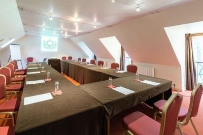 Vue nocturne d'une maison en bois éclairée, entourée d'arbres illuminés, sous un ciel nuageux avec la lune visible.