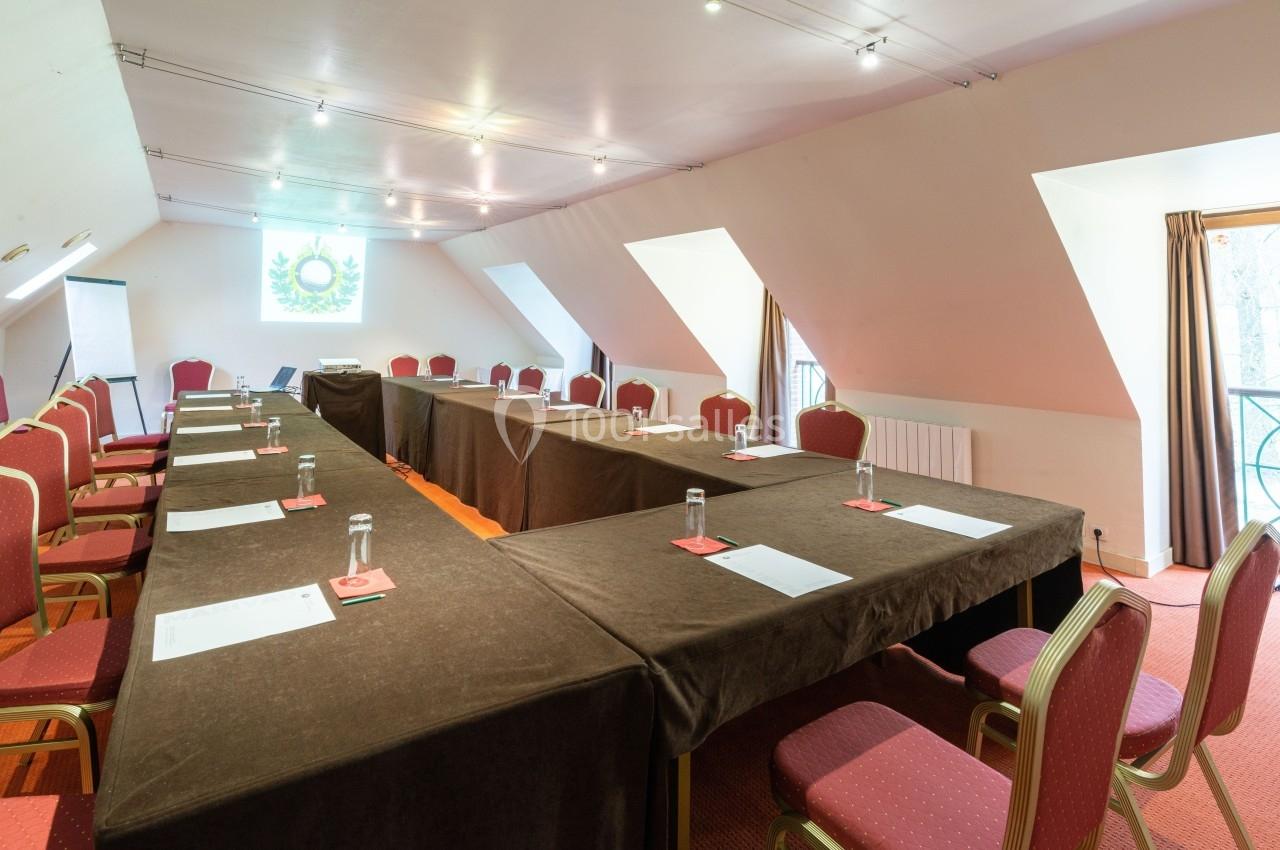 Salle de réunion lumineuse avec tables disposées en U, chaises rouges et matériel de conférence sur les tables.