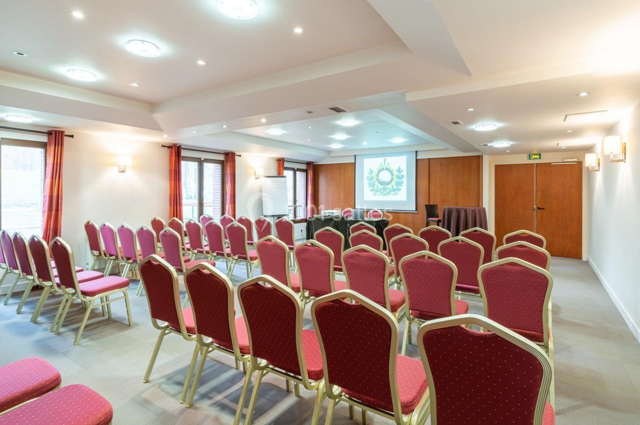 Salle de conférence lumineuse avec des rangées de chaises rouges, un écran de projection et un tableau blanc.