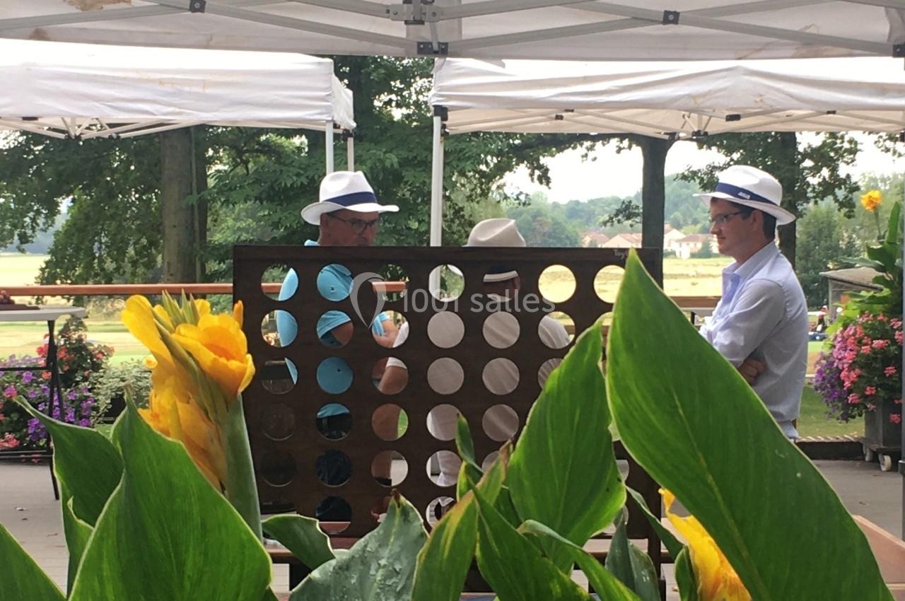 Deux hommes jouent à un jeu de puissance 4 géant sous des tonnelles blanches, entourés de plantes et de fleurs.