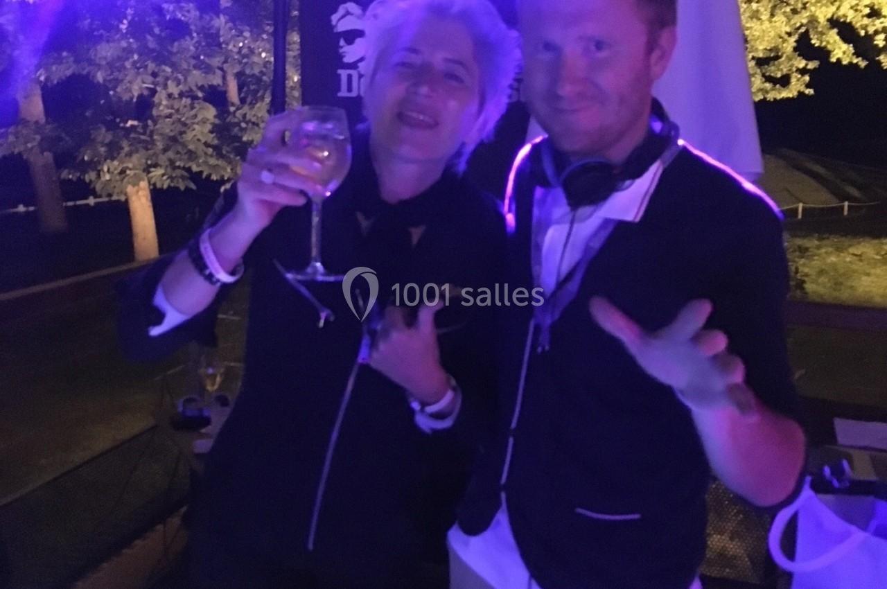 Deux personnes souriantes derrière une table de mixage éclairée, dans une ambiance nocturne festive.