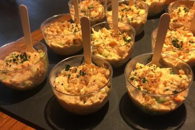 Vue nocturne d'une maison en bois éclairée, entourée d'arbres illuminés, sous un ciel nuageux avec la lune visible.