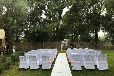 Espace extérieur décoré avec arche florale, deux chaises transparentes et fond blanc sous une tente.