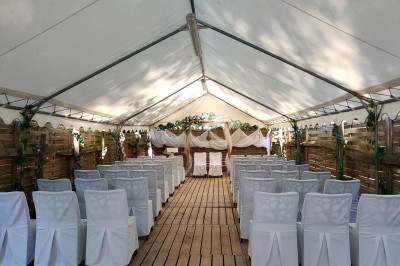 Espace extérieur décoré avec arche florale, deux chaises transparentes et fond blanc sous une tente.