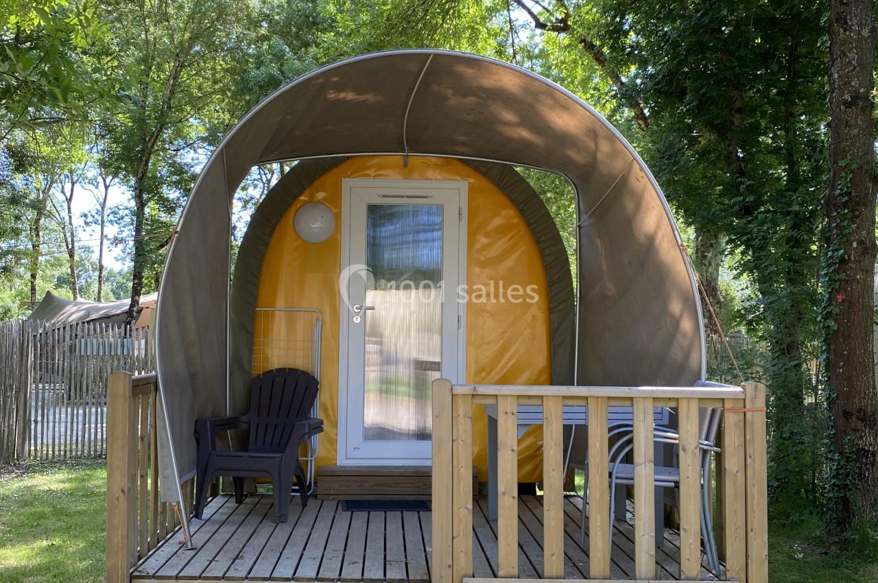 Hébergement insolite en forme de tente avec terrasse en bois, entouré d'arbres et situé dans un espace naturel.