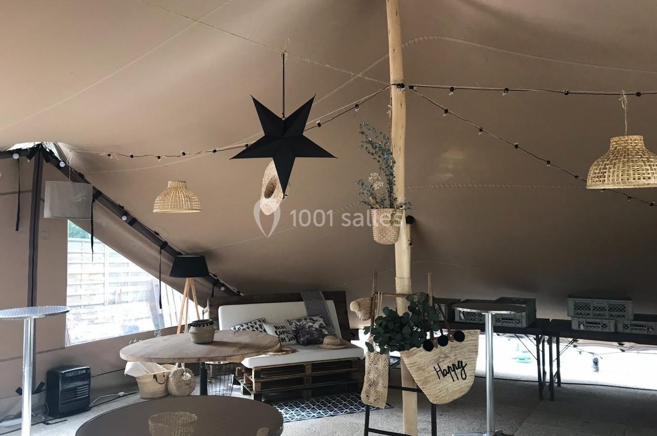 Intérieur d'une tente aménagée avec des meubles en bois, des guirlandes lumineuses et des décorations suspendues.