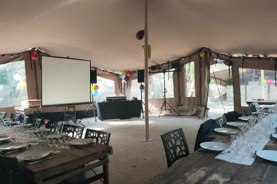 Espace extérieur décoré avec arche florale, deux chaises transparentes et fond blanc sous une tente.