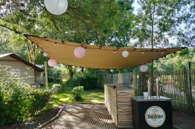 Espace extérieur décoré avec arche florale, deux chaises transparentes et fond blanc sous une tente.