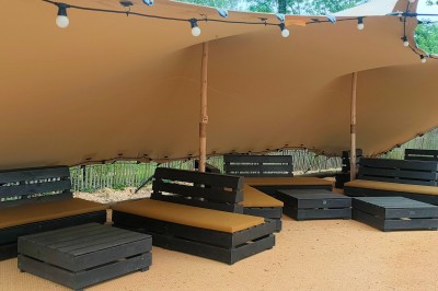 Espace extérieur décoré avec arche florale, deux chaises transparentes et fond blanc sous une tente.