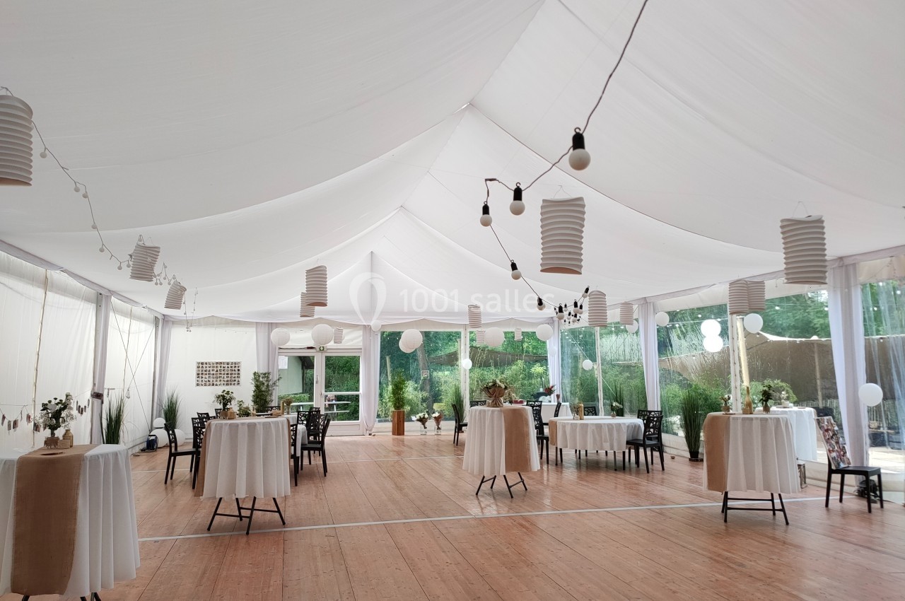 Salle de réception lumineuse sous une tente blanche avec tables rondes décorées et lanternes suspendues.