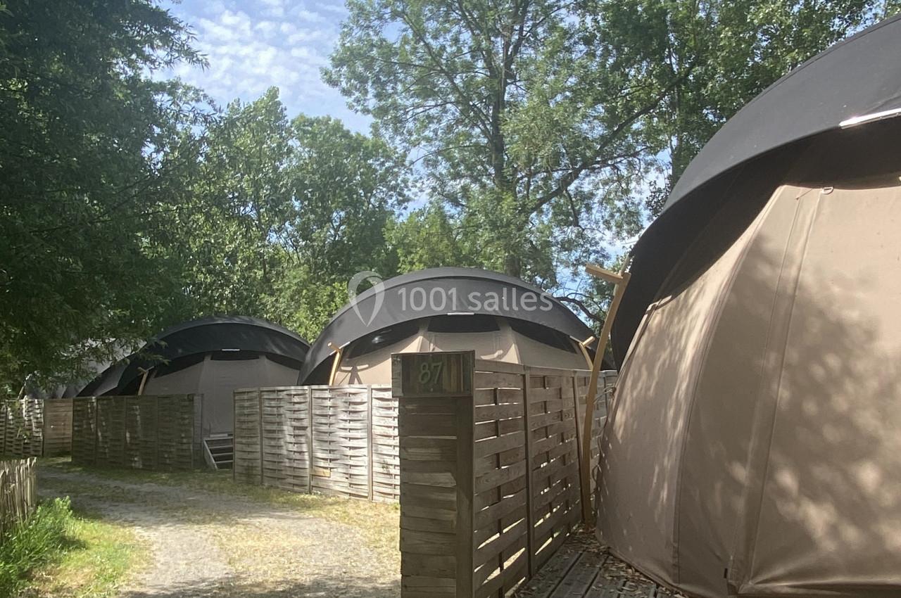Trois tentes en toile beige sur des plateformes en bois, entourées d'arbres et d'une allée en gravier.