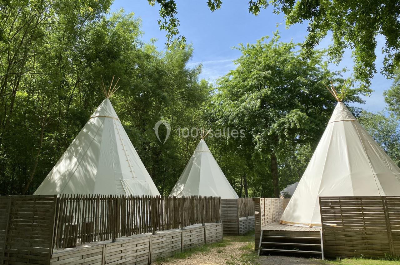 Trois tipis blancs entourés de clôtures en bois, situés dans un cadre verdoyant sous un ciel dégagé.