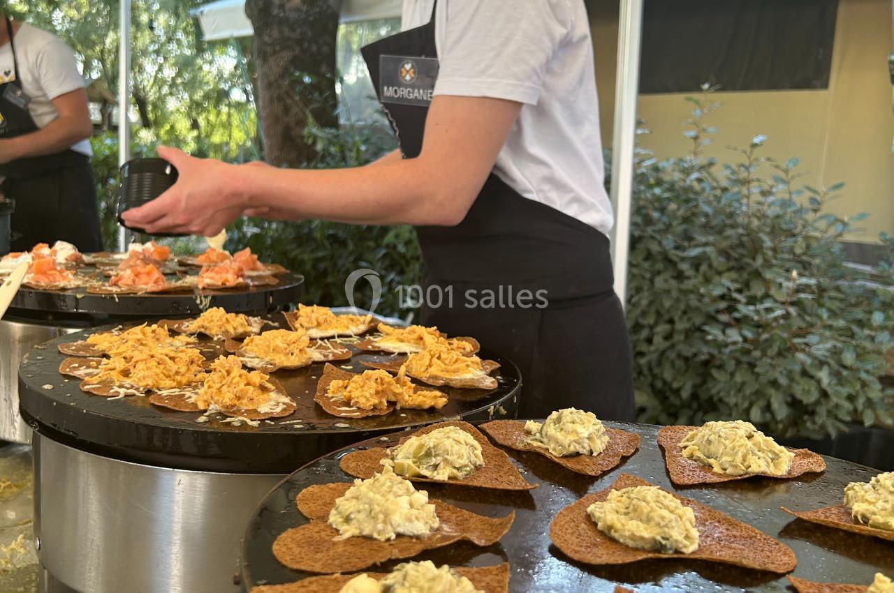 Une cuisinière prépare des galettes garnies sur des plaques chauffantes lors d'un événement en extérieur.