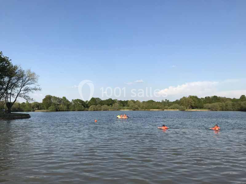 Des personnes nagent et pagaient sur un lac entouré d'arbres sous un ciel dégagé.