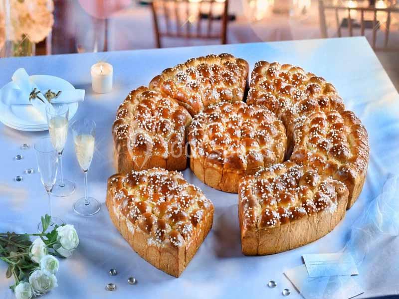 Brioche en parts disposée sur une table décorée avec des fleurs, des bougies et des flûtes de champagne.