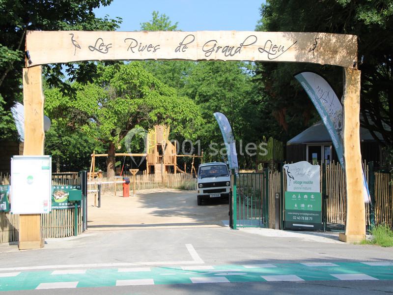 Entrée d'un site touristique avec une arche en bois, des panneaux d'information et un espace naturel en arrière-plan.