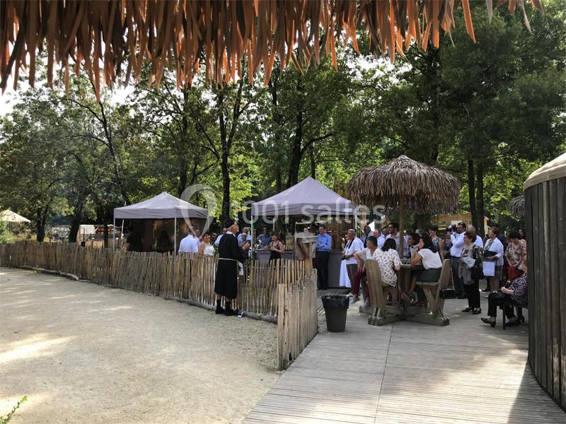 Groupe de personnes réunies en extérieur sous des tonnelles, entourées d'arbres et de clôtures en bois.