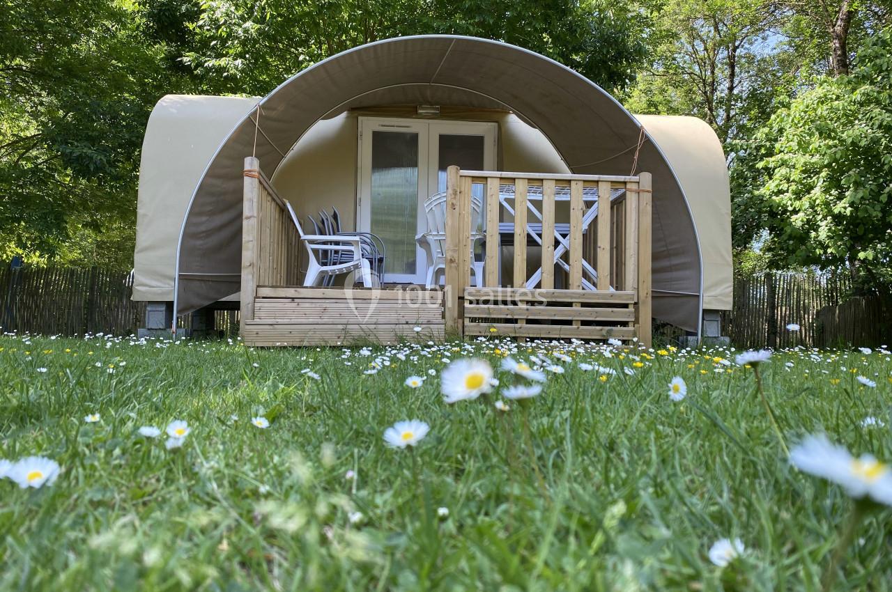 Tente lodge avec terrasse en bois, entourée de pelouse et de marguerites, située dans un environnement arboré.