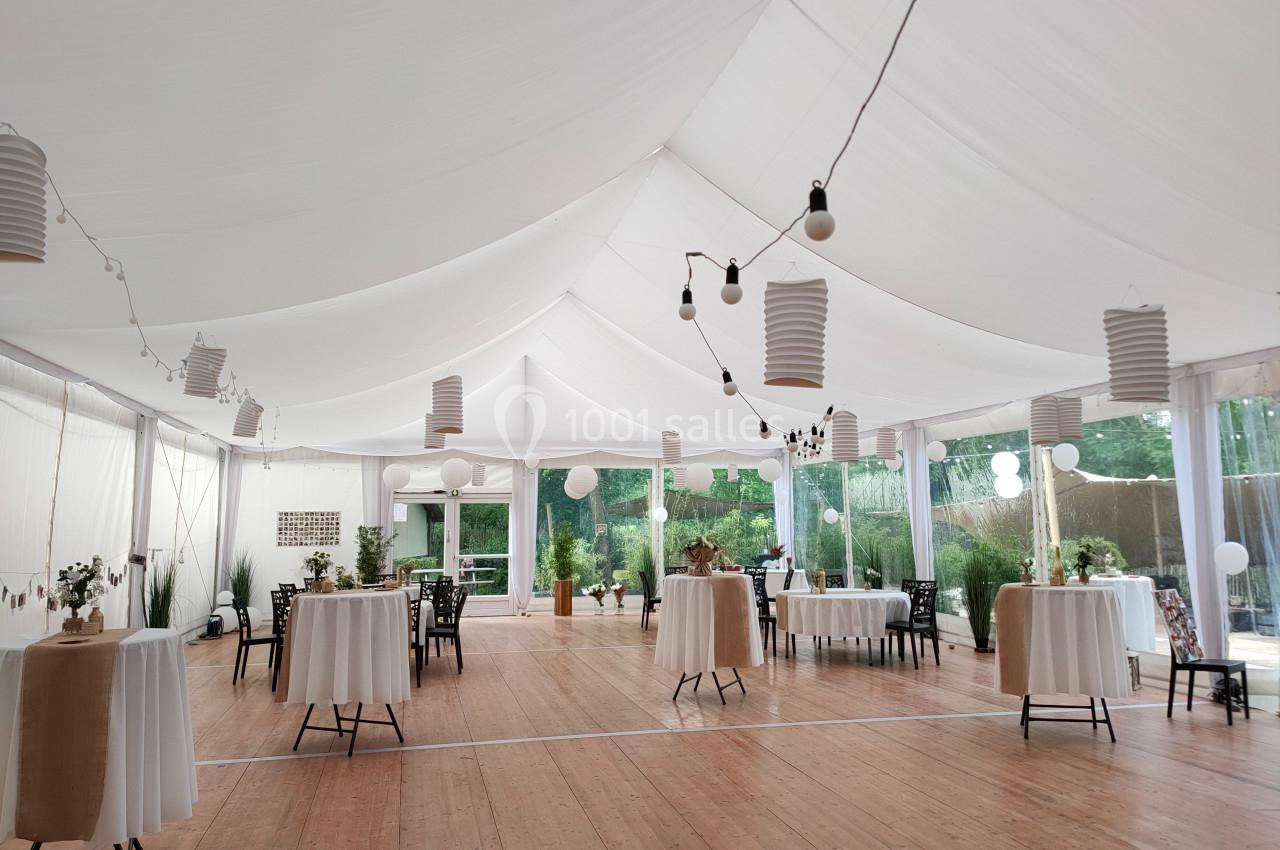Salle de réception lumineuse sous une tente blanche, avec tables rondes décorées et lanternes suspendues.