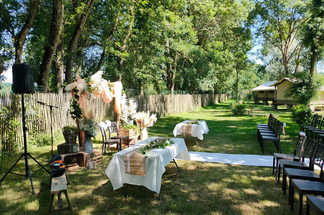 Cérémonie en plein air avec chaises alignées, tables décorées et arche florale dans un cadre verdoyant.