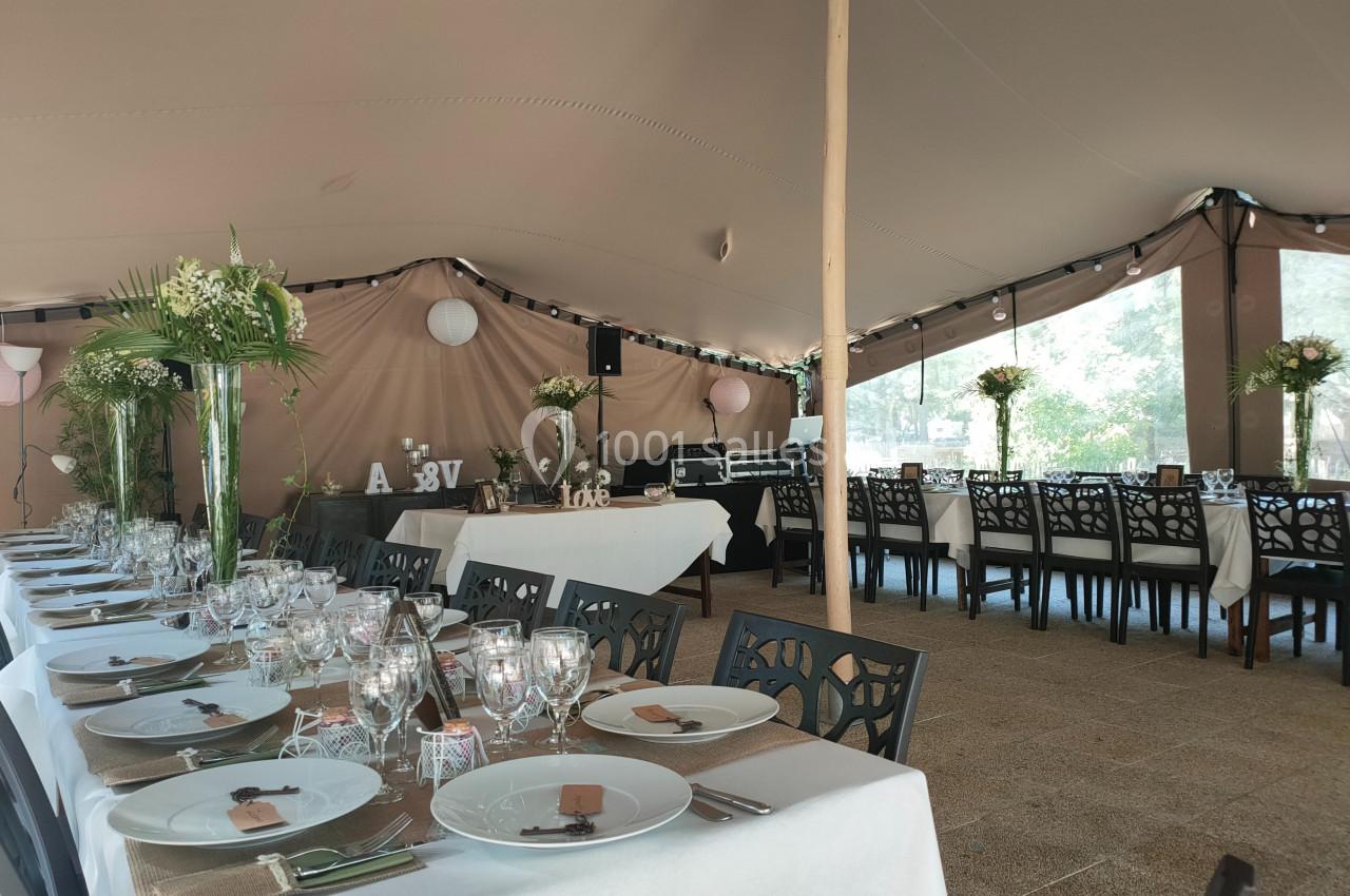 Salle de réception décorée pour un événement, avec tables dressées, nappes blanches et arrangements floraux.