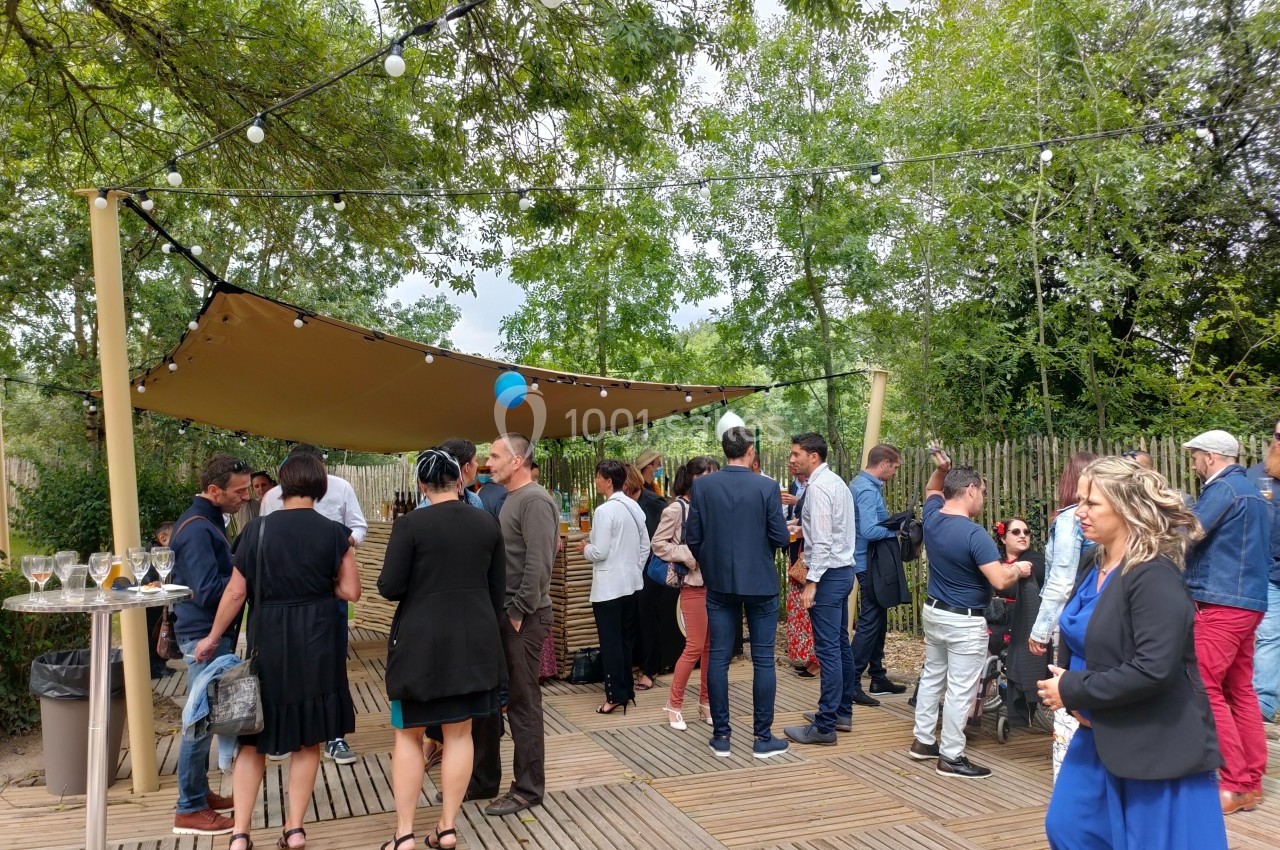 Groupe de personnes discutant sous une toile tendue avec des guirlandes lumineuses, dans un espace extérieur boisé.