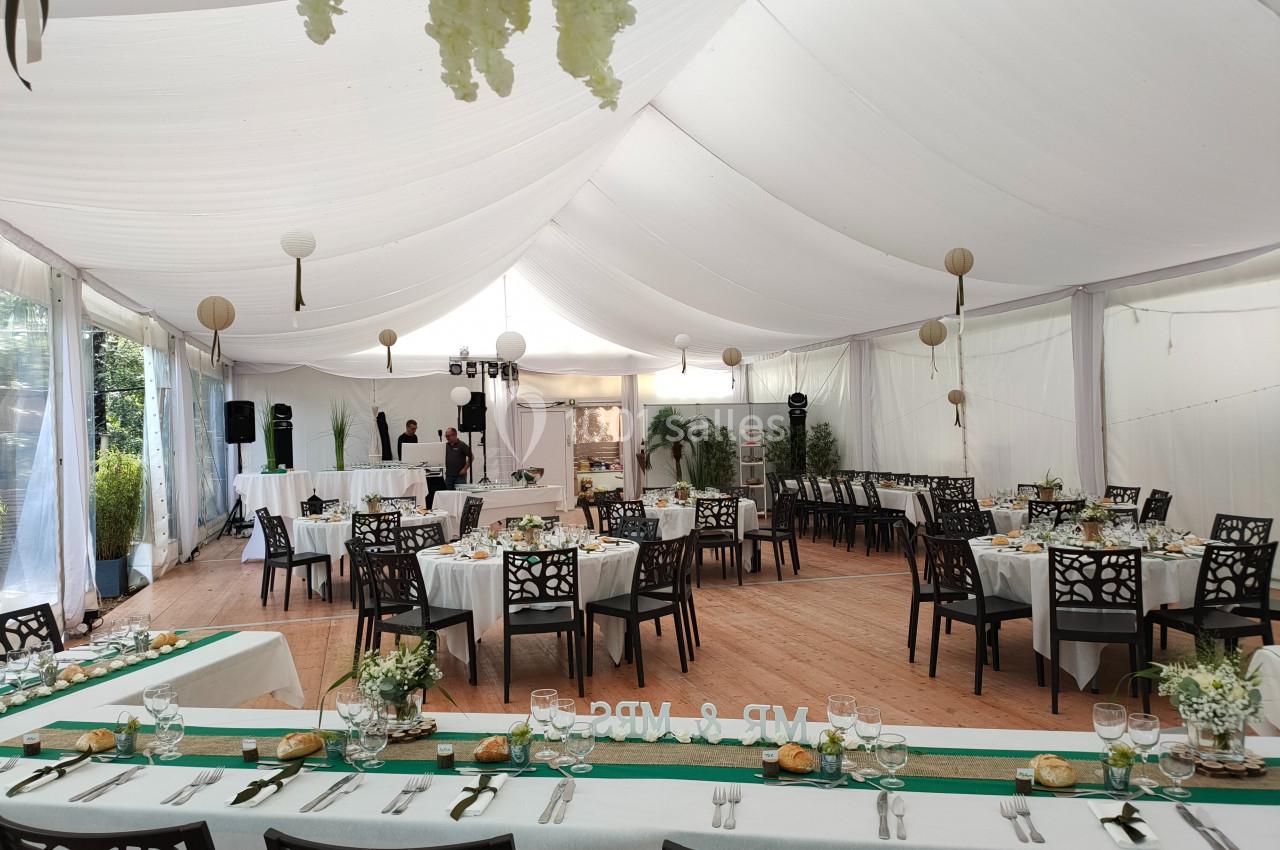 Salle de réception décorée avec des tables dressées, nappes blanches et touches de vert, sous une tente blanche.