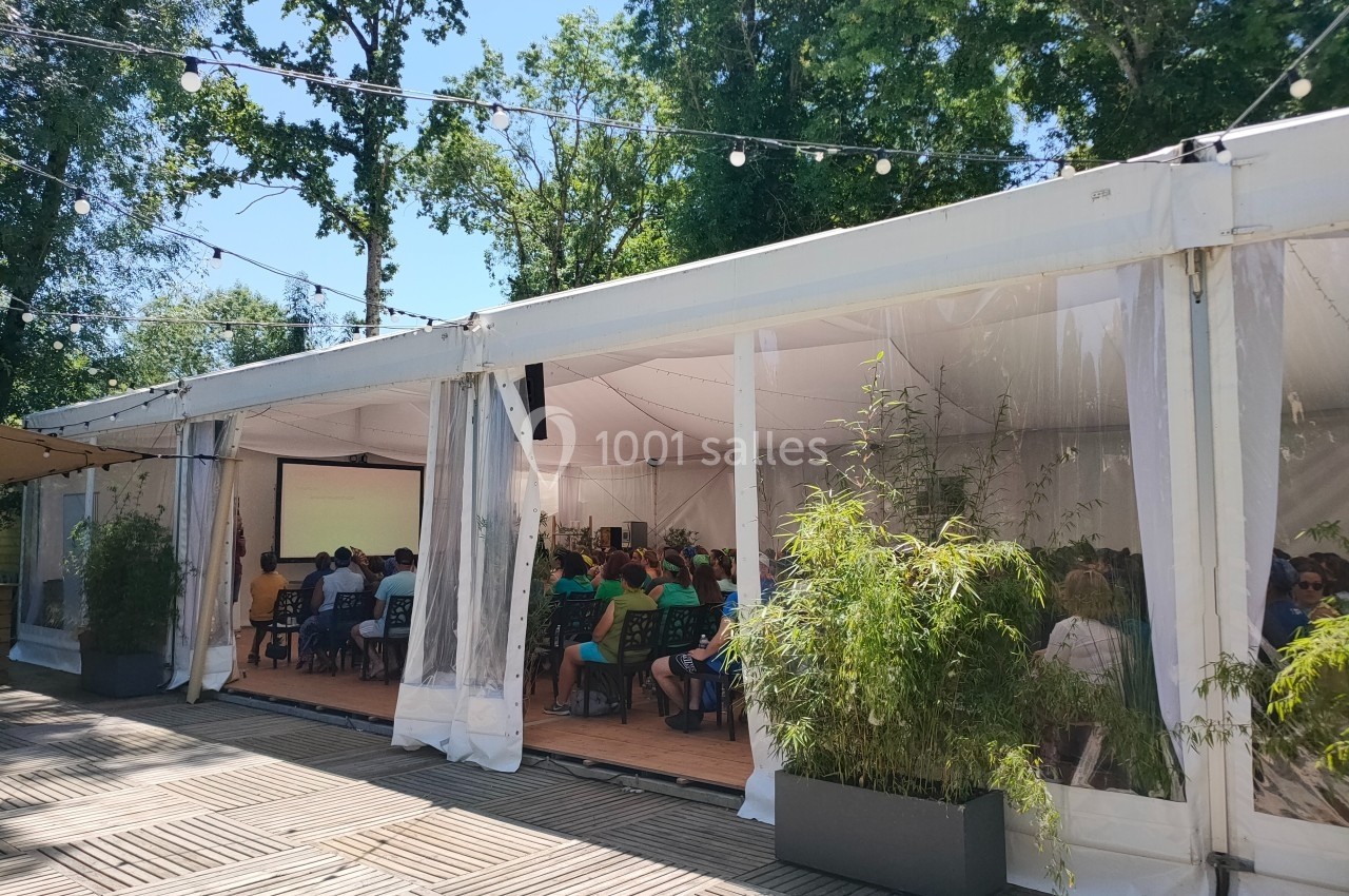Vue extérieure d'une tente transparente abritant un événement avec des participants assis, entourée de végétation.