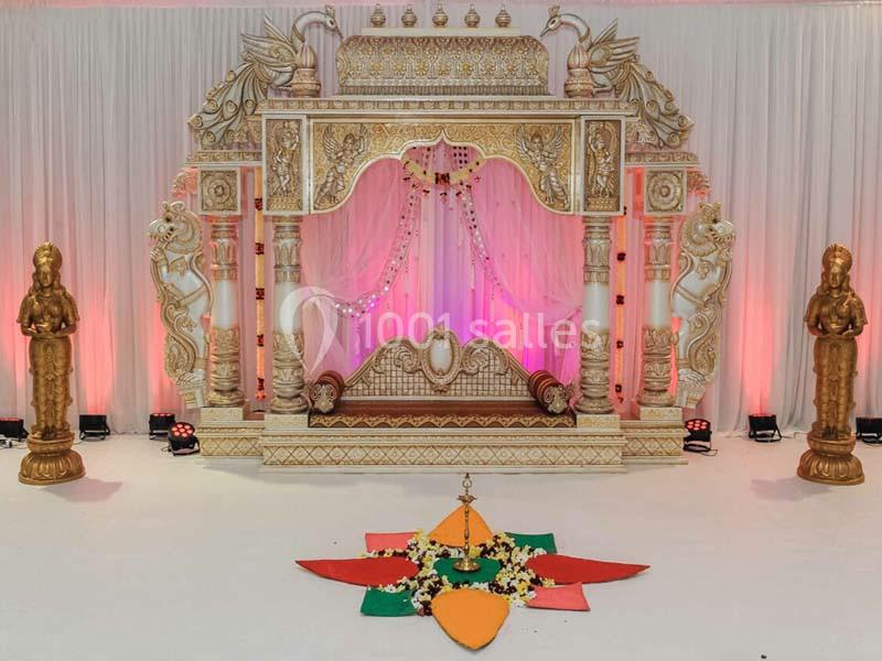 Décor de mariage traditionnel avec arche ornée, statues dorées et motif coloré au sol devant un rideau blanc.