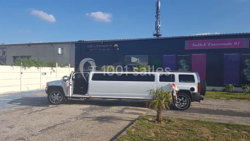 Limousine blanche stationnée devant une salle de réception avec des palmiers et un ciel dégagé en arrière-plan.