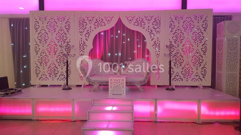 Décor de scène avec canapé blanc sculpté, panneaux ornés de motifs arabesques et éclairage rose lumineux.